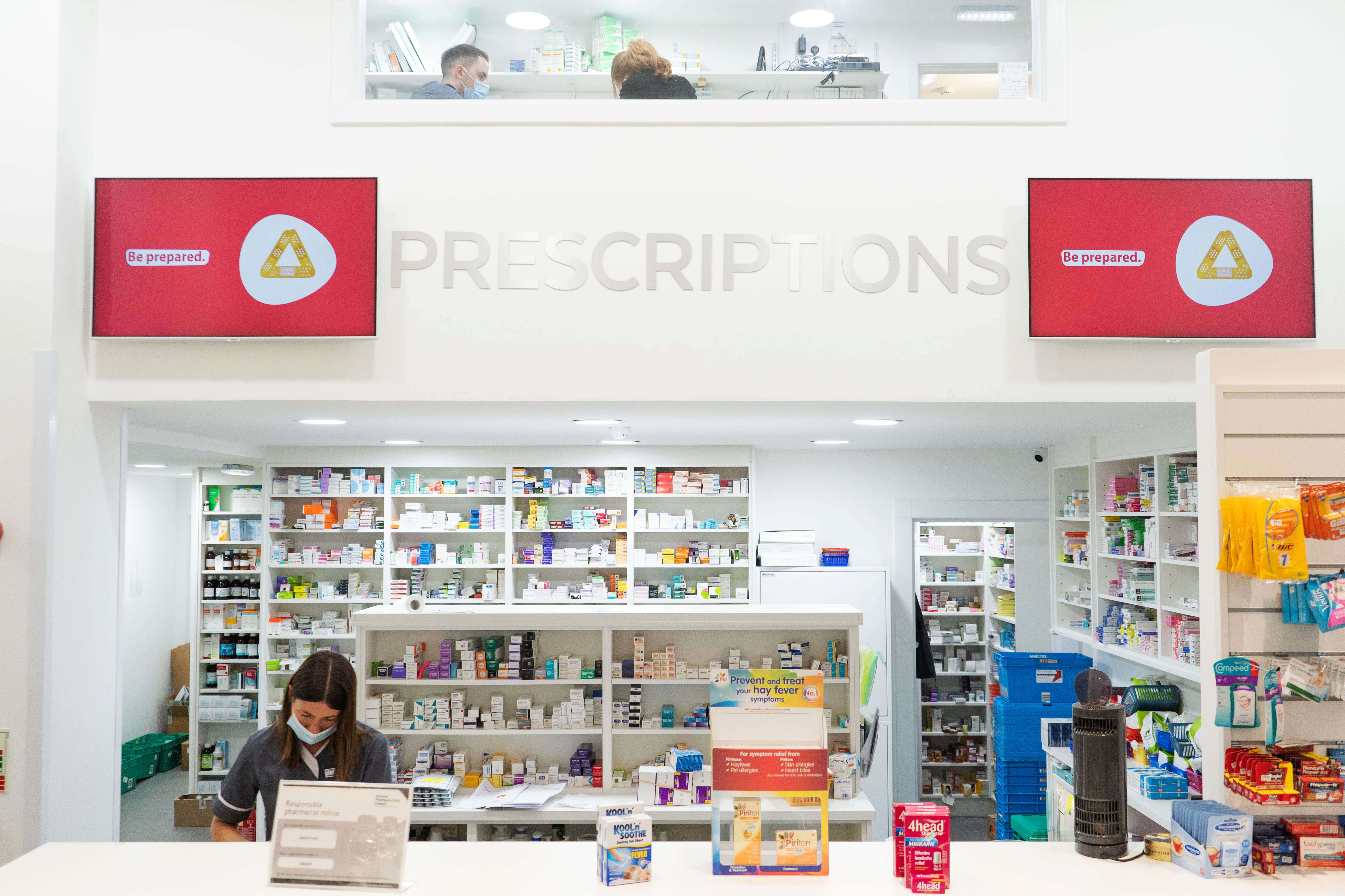 photo of front desk at a pharmacy, with woman behind electronic till and medication on shelves behind her