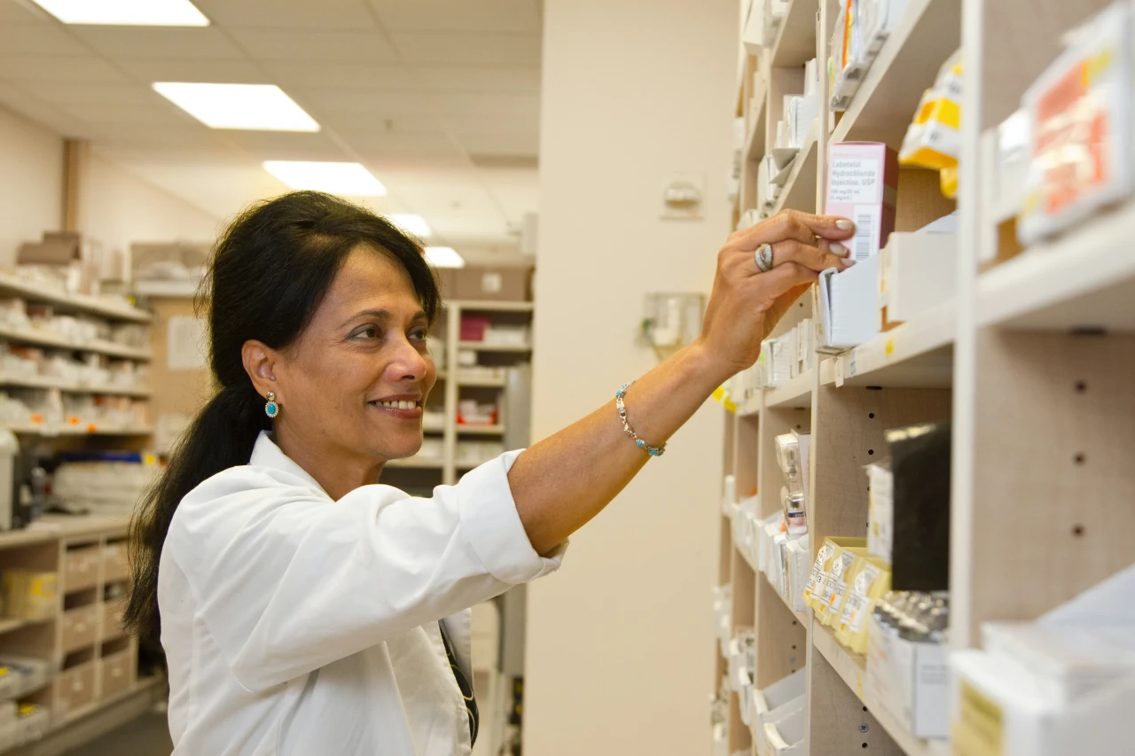 Female pharmacist in white coat smiling whilst picking some medication off shelf