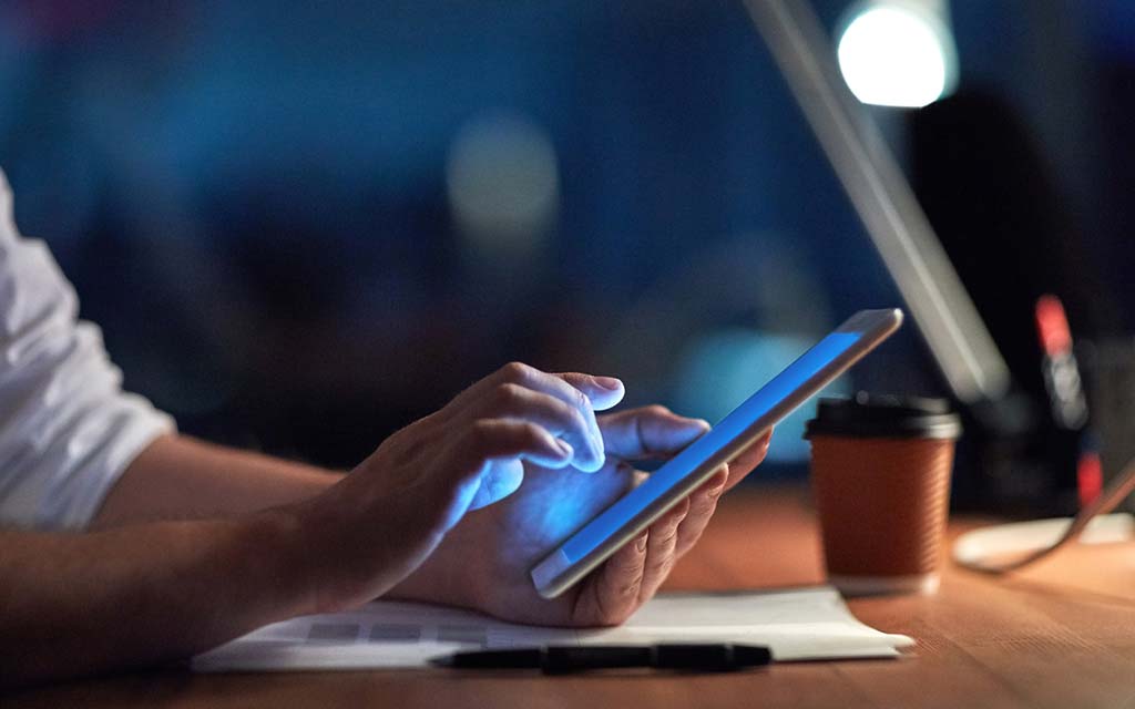 Close up of hand holding a tablet whilst other hand scrolls on the screen